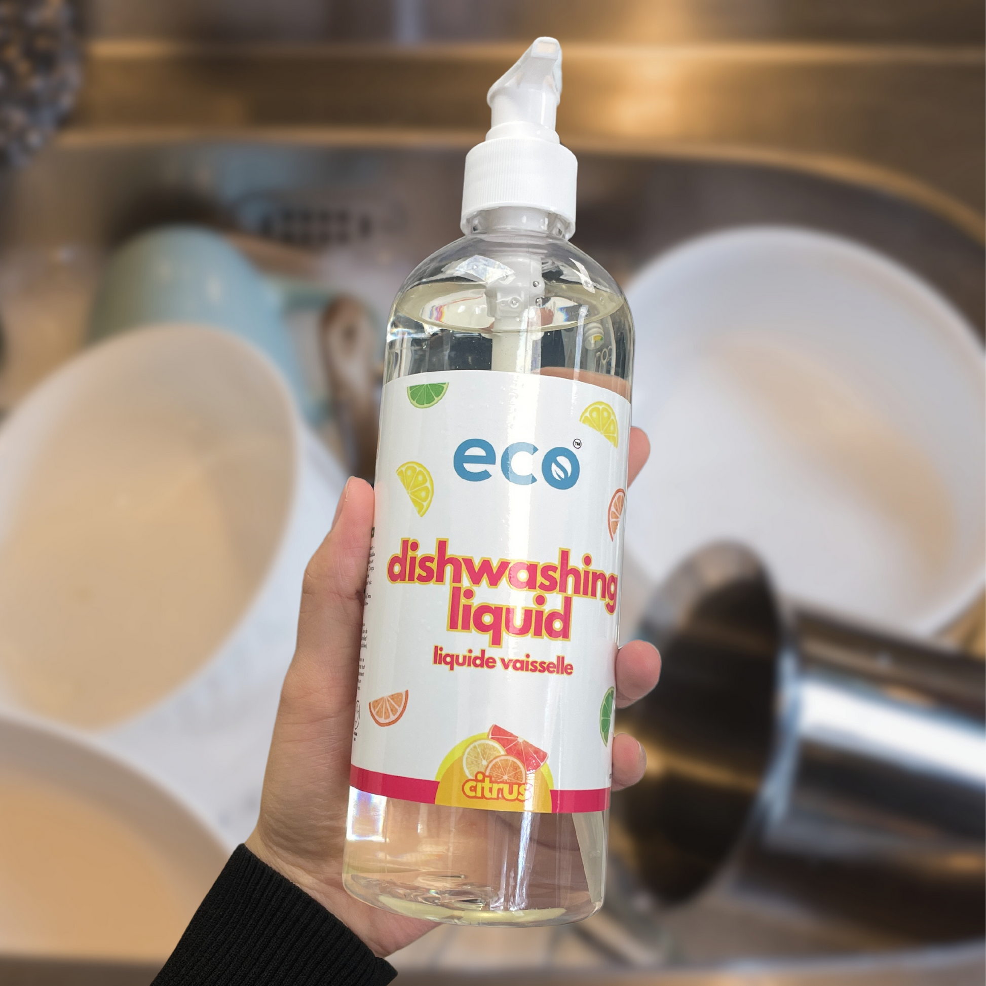 A bottle of eco dish soap citrus held in front of dirty dishes, for an eco-friendly and sustainable home.