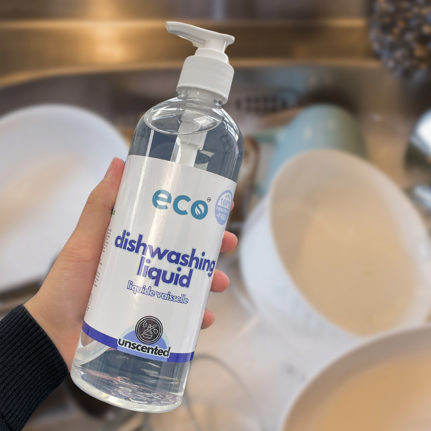 A bottle of eco dish soap unscented held in front of a sink of dishes, for an eco-friendly and sustainable kitchen.