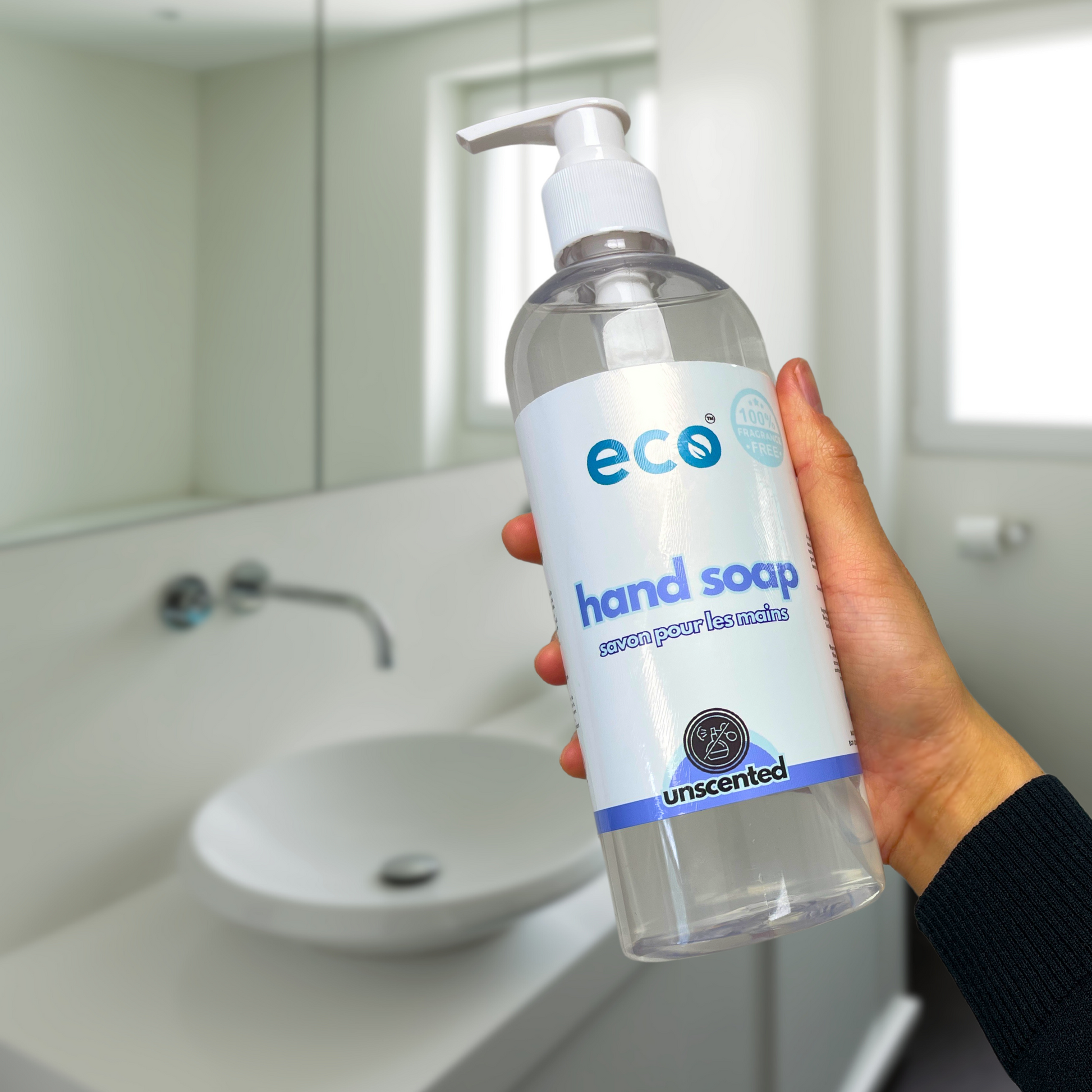 A bottle of eco hand soap unscented held in front of a washroom sink, for an eco-friendly and plant-based home.